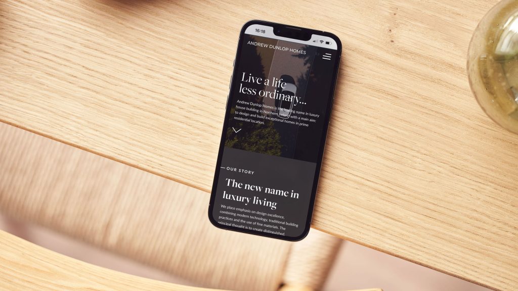 We Are Kaizen Andrew Dunlop Homes website on a smartphone sitting on a wooden table